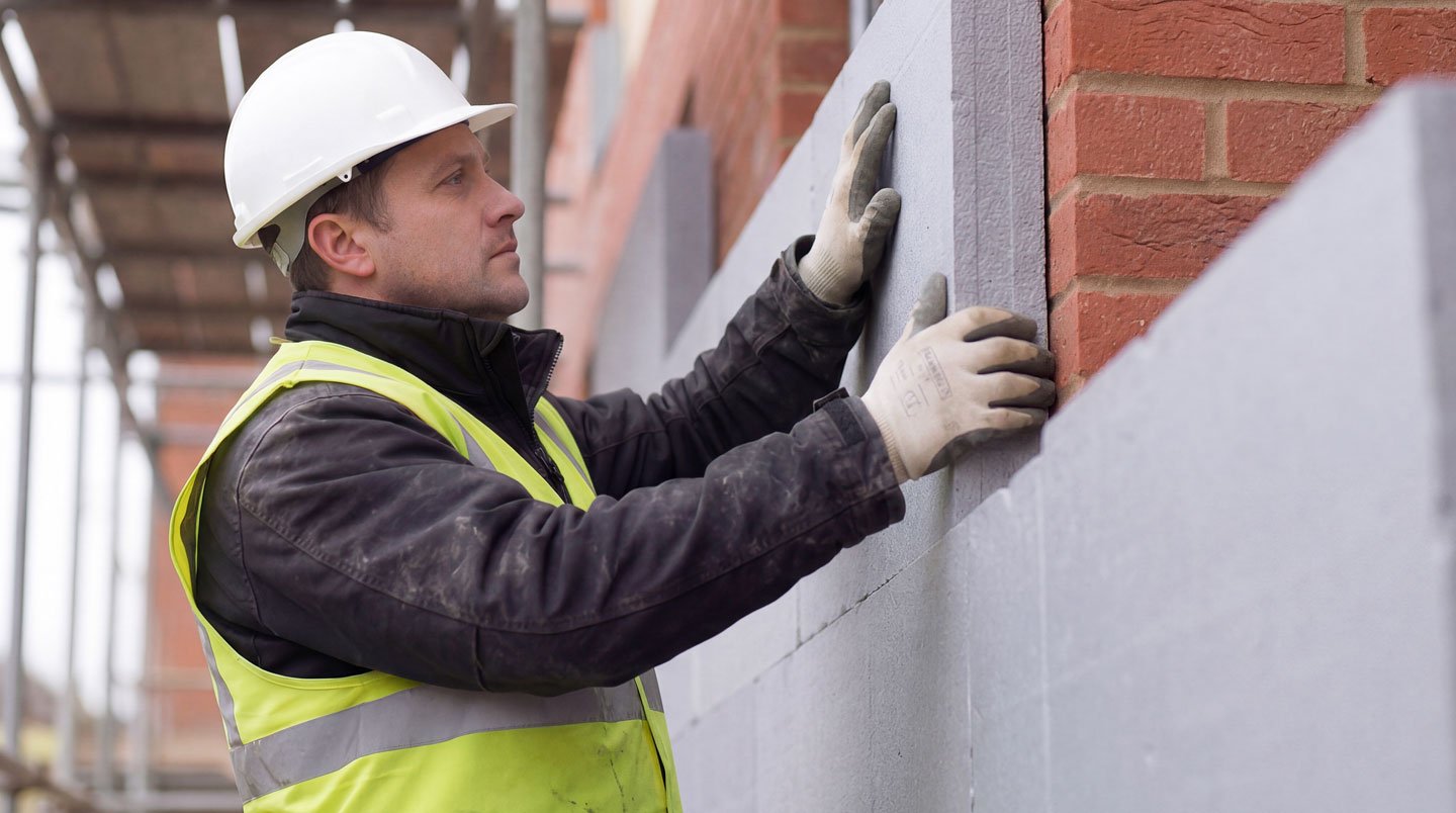 Artisan installant des panneaux d'isolation thermique haute performance sur l'ossature murale d'une extension de maison